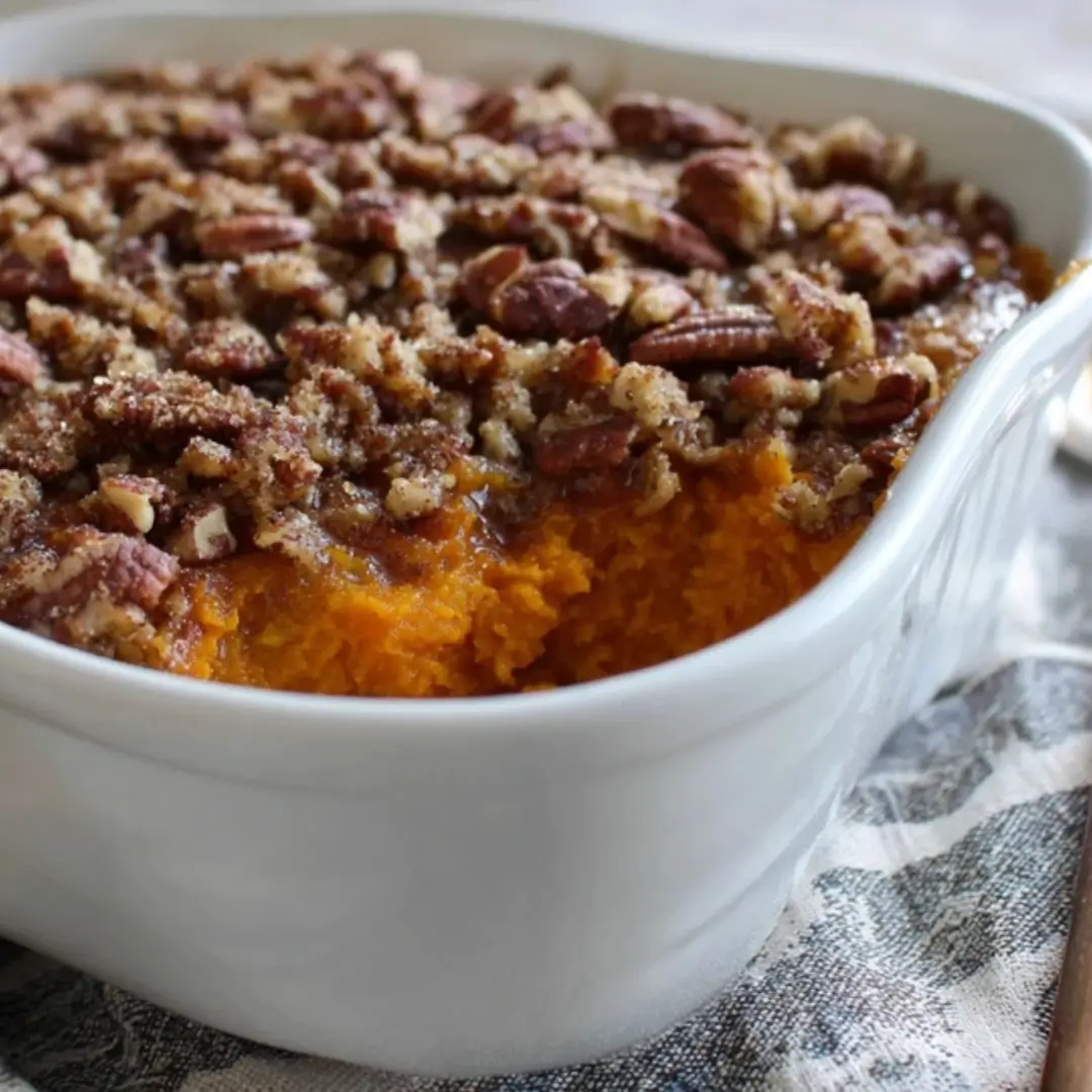 A white ceramic baking dish filled with mashed sweet potato casserole topped with a thick layer of toasted brown sugar and pecan crumble.