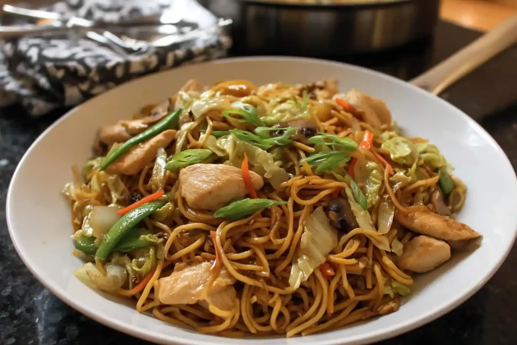 A close-up shot of a white bowl filled with delicious homemade Pancit Canton with chicken, cabbage, and other vegetables.