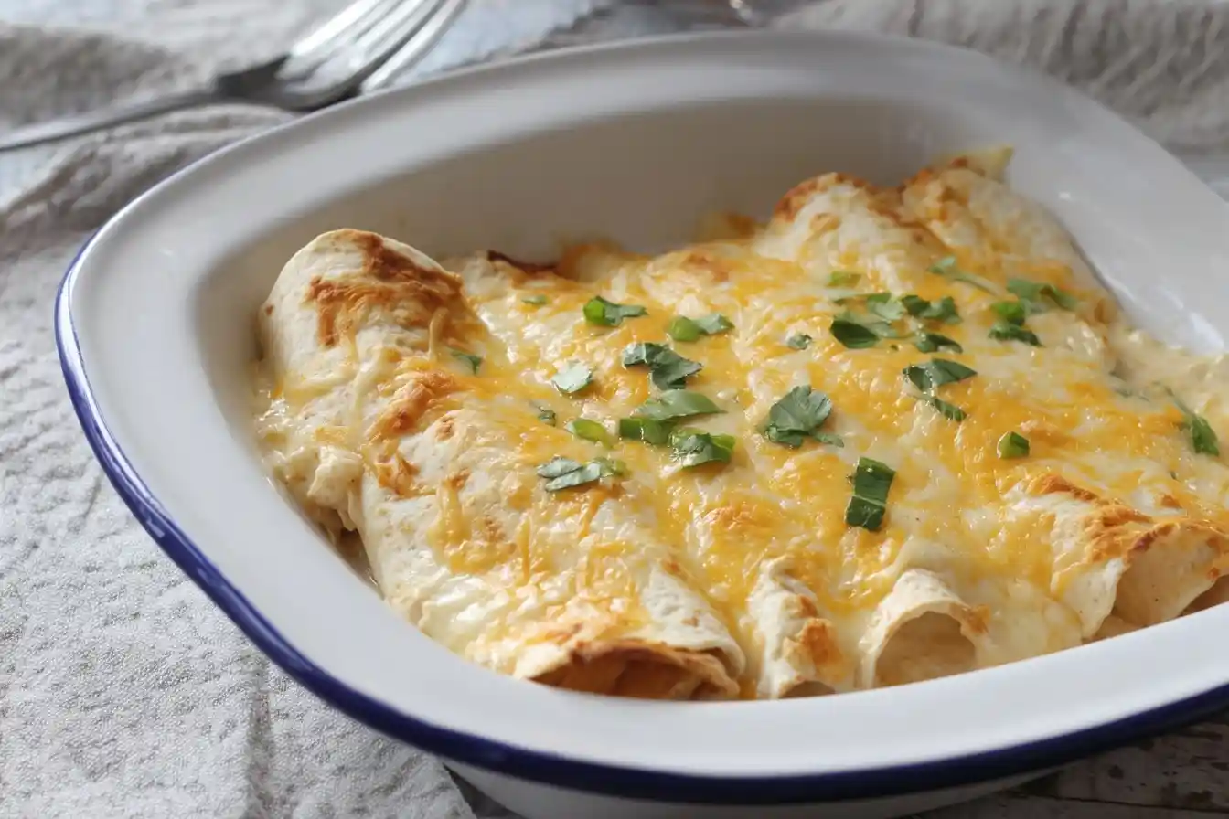 A close-up of creamy chicken enchiladas in a white baking dish, topped with melted cheese and garnished with fresh cilantro.