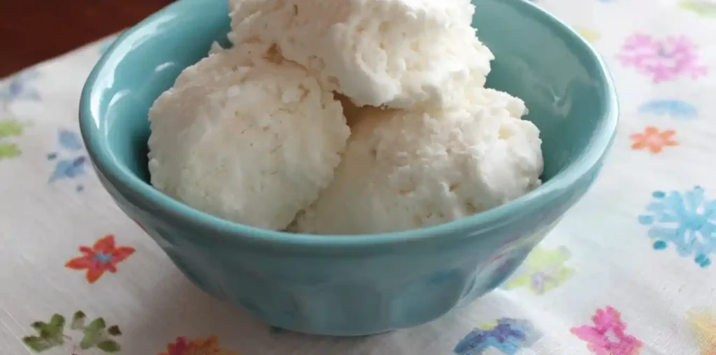 A light blue bowl filled with several scoops of fluffy, white Snow Ice Cream on a floral napkin.