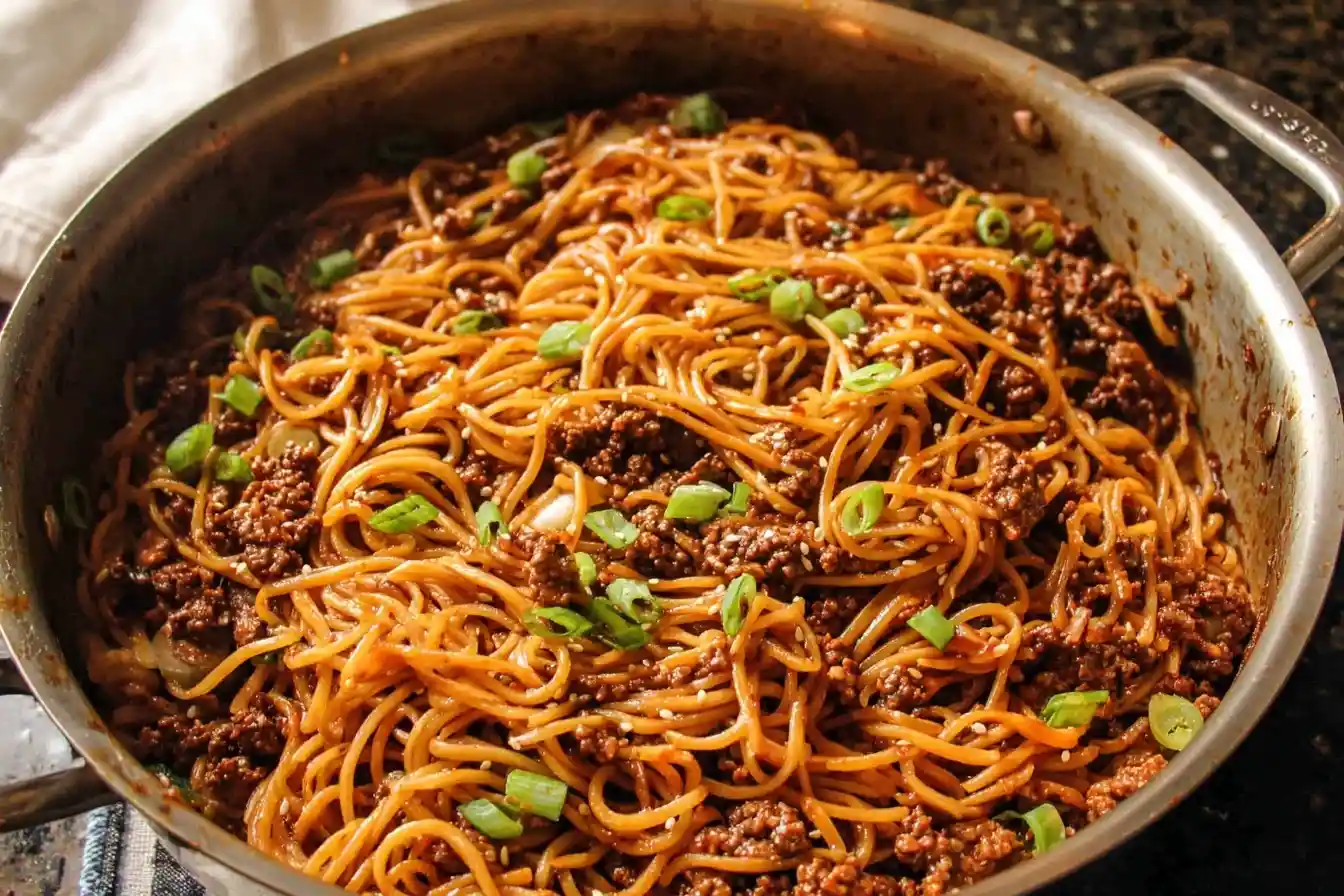A large skillet filled with delicious spicy noodles, ground meat, and a garnish of fresh green onions and sesame seeds.