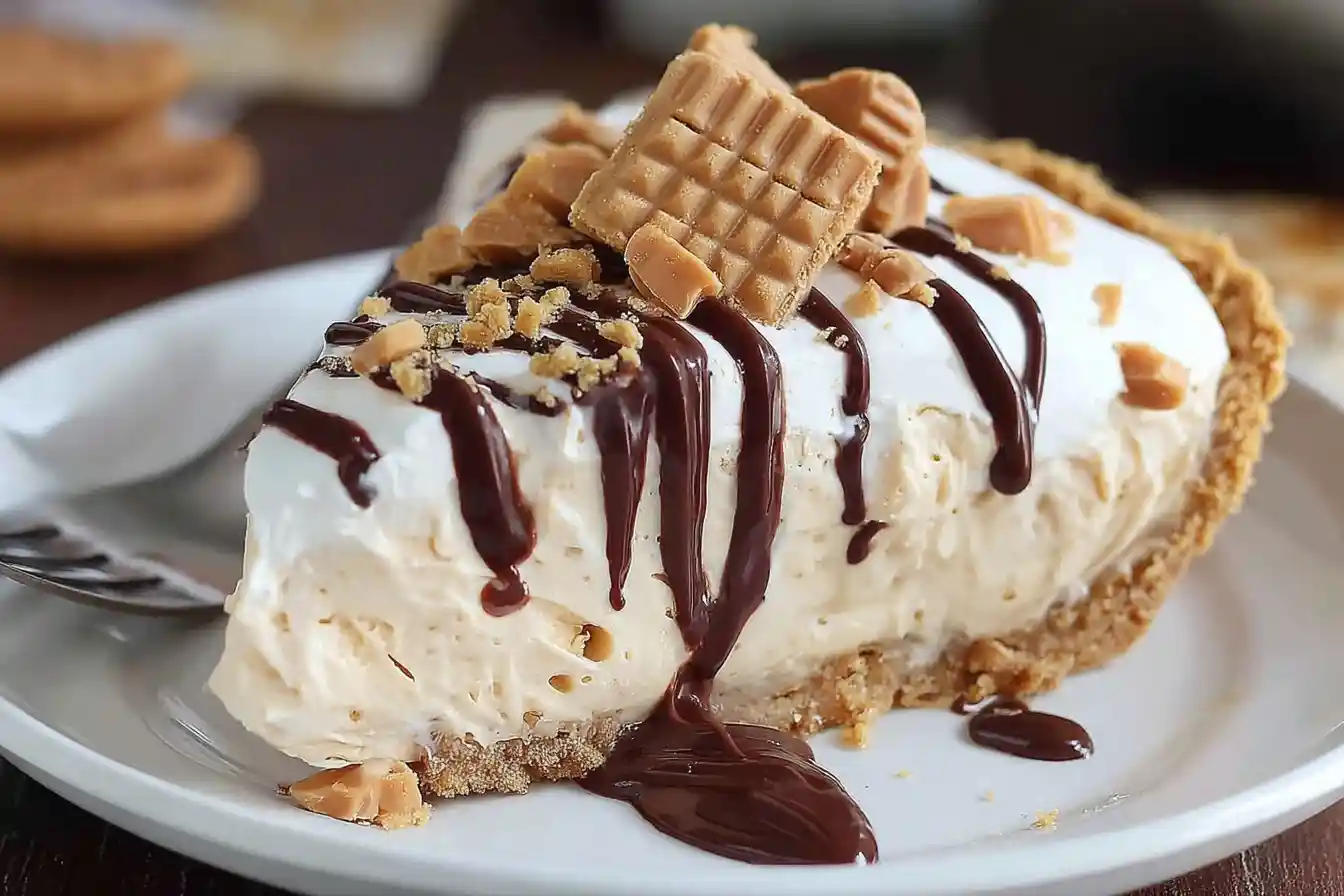 Close-up of a slice of Nutter Butter Pie with whipped cream, chocolate drizzle, and cookie toppings on a white plate.