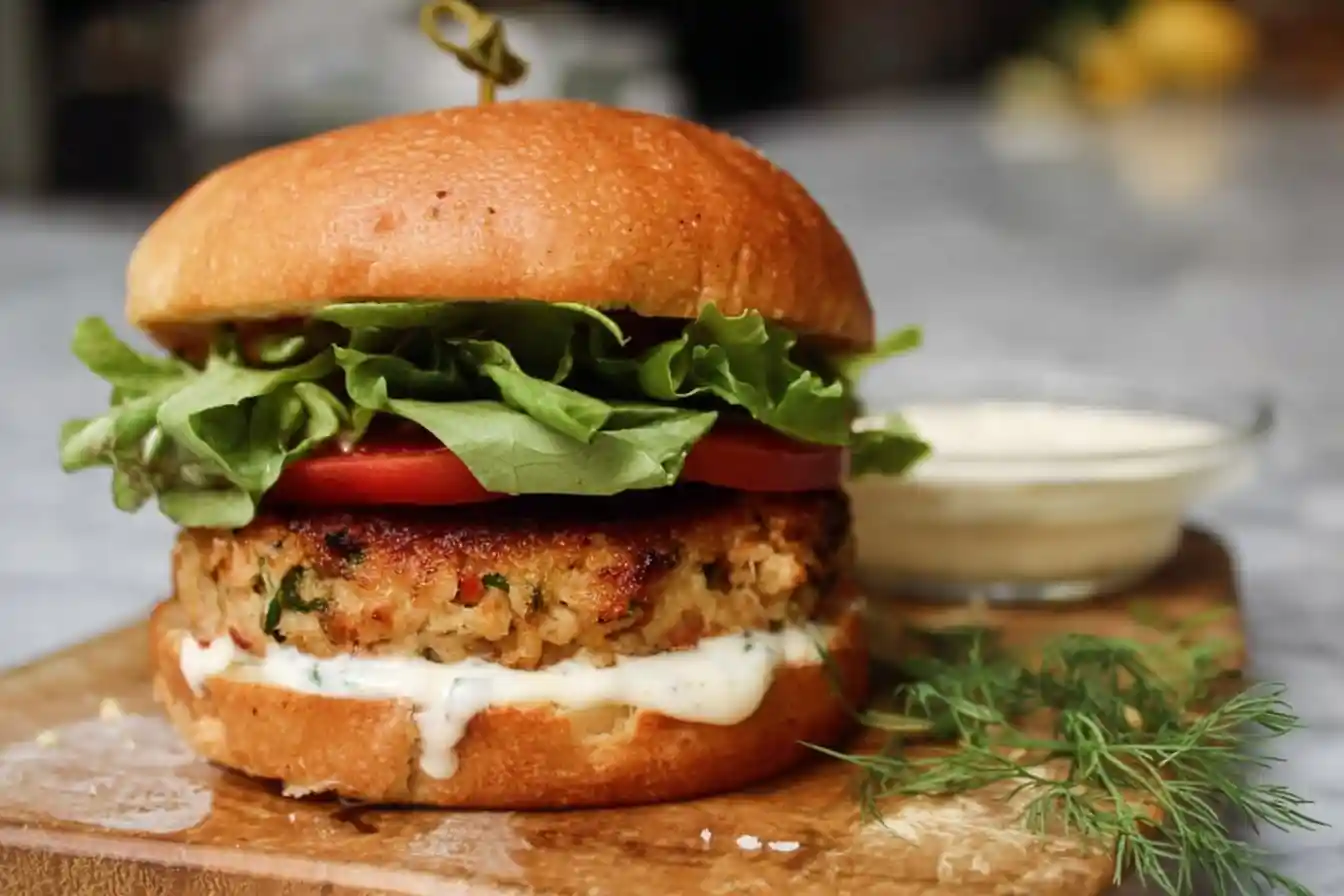 Juicy salmon burger on a toasted bun with lettuce, tomato, and creamy sauce on a wooden board