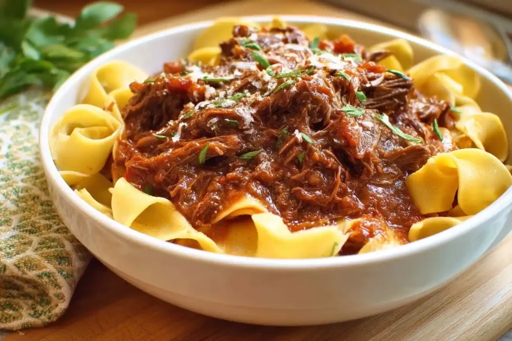 A white bowl filled with wide noodles topped with savory Beef Ragu, fresh herbs, and grated cheese.