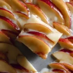 A square slice of {{ $('Fetch Recipe Data').first().json["Main Keyword"] }} topped with fresh apples and glaze.