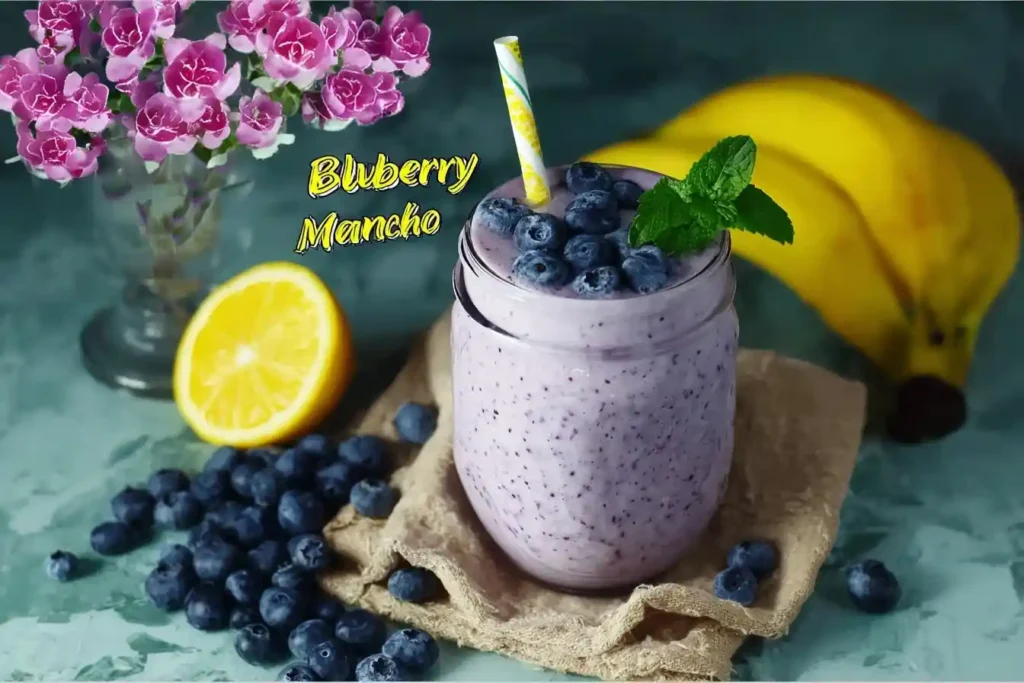 A glass jar filled with a thick blueberry smoothie, topped with fresh berries and mint, next to bananas and a lemon half.