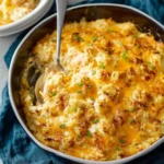 A serving spoon resting in a baked {{ $('Fetch Recipe Data').first().json['Main Keyword'] }} with melted cheese and chives.