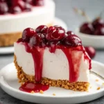 A close-up of a delicious slice of cherry cheesecake with glossy cherry topping dripping down the sides on a white plate.
