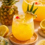 A cold glass of {{ $('Fetch Recipe Data').first().json["Main Keyword"] }} garnished with a pineapple wedge, cherry, and fresh lemons.