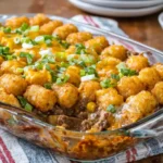 A glass baking dish filled with cheesy tater tot casserole, ground beef, and green onions.